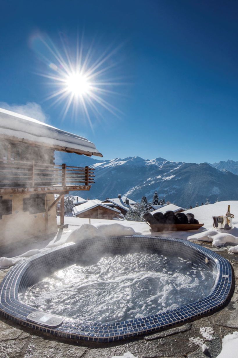 Outdoor hot tub with chalet building behind and mountain views at Chalet Chouqui. Part of the luxury chalet club collection.