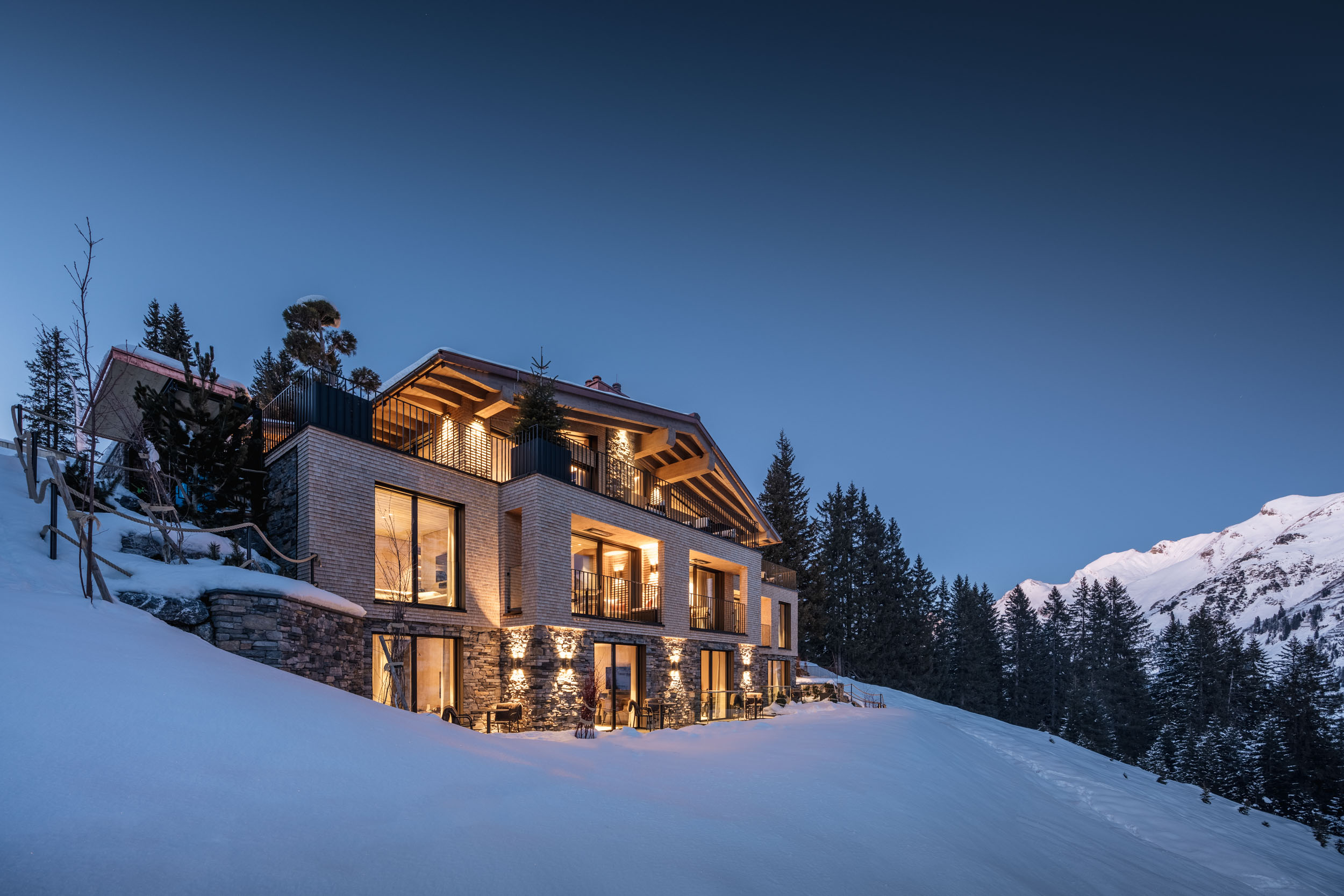 Le Chalet in Lech on the side of the mountain at night. Part of the luxury chalet club collection